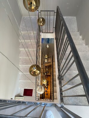 Un escalier avec une rampe en métal, une série de luminaires suspendus et une vue sur un espace intérieur doté d’une porte en bois.