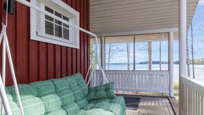 En overdækket veranda med en grønstribet sofa, et hvidt gelænder og udsigt over en sø.