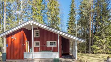Eine rote Holzhütte mit Veranda, weißen Geländern und freiem Blick auf den umliegenden Wald.