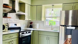 A kitchen with light green cabinets, a stainless steel range, a built-in oven, a sink, and a window with blinds.