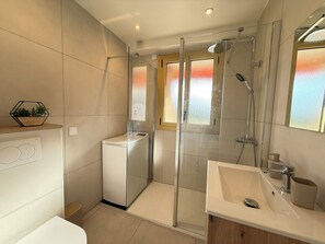 Ein modernes Badezimmer mit einer Duschkabine aus Glas, einer integrierten Waschmaschine und einem großen Waschbecken mit Spiegel.