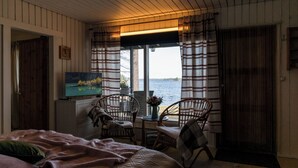 Een kamer met een bed, een televisie, een raam met gordijnen en uitzicht op het water.