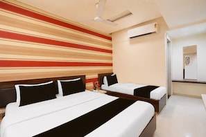 Habitación de hotel con dos camas, ventilador de techo, aire acondicionado y un pasillo que conduce a un baño.