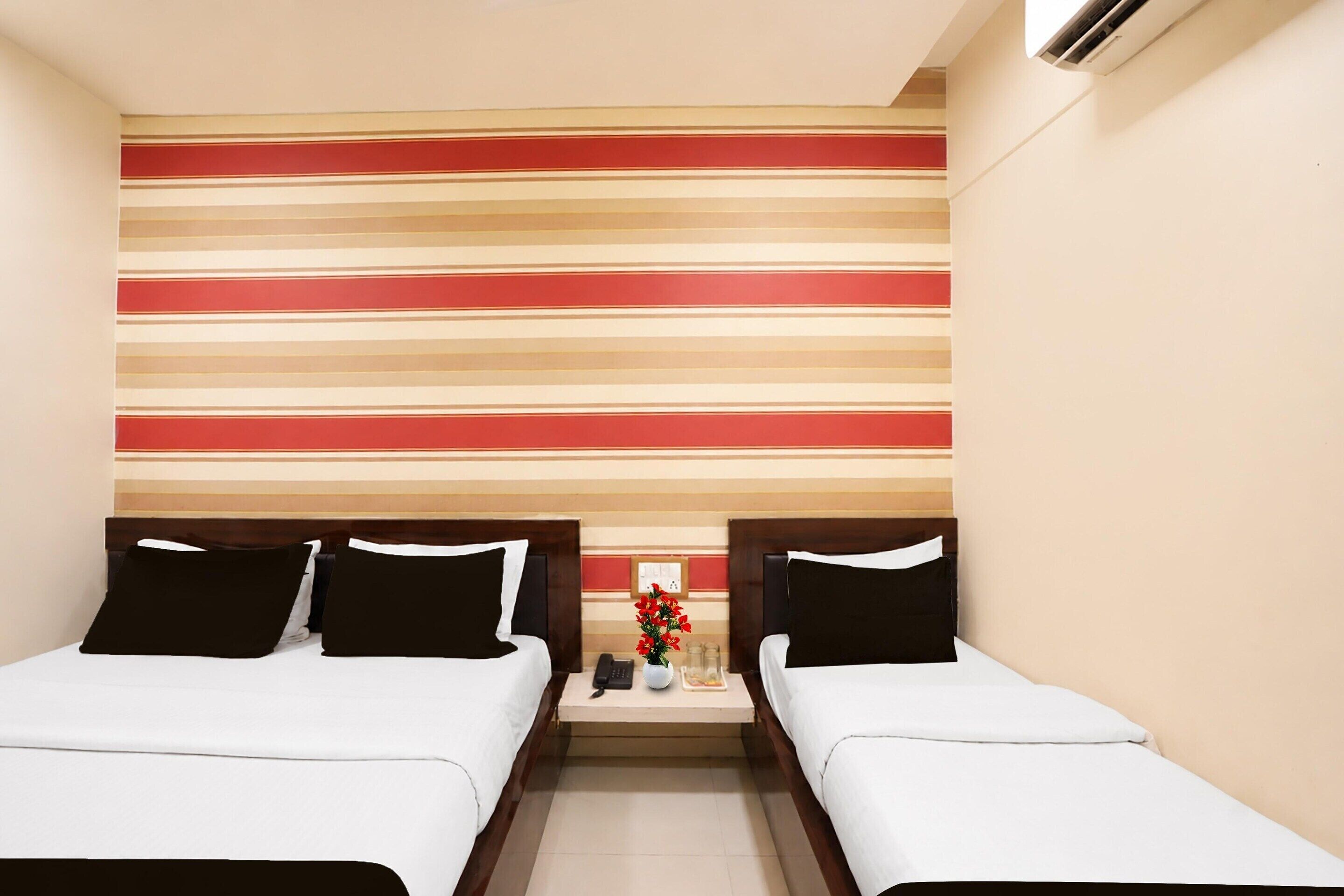 A hotel room with two beds, a nightstand with a phone and a vase of flowers, and a striped wall design.
