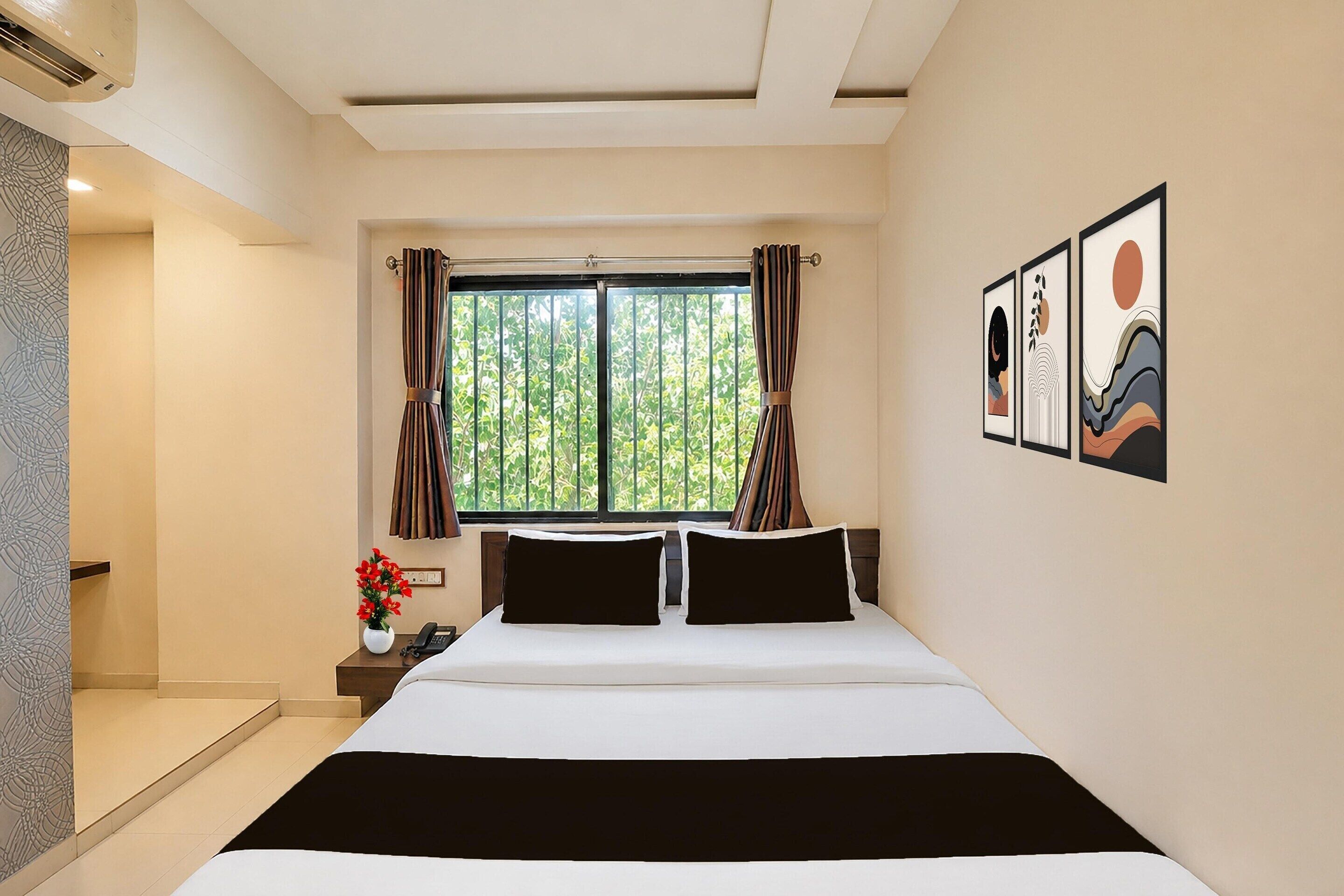 A hotel room with a bed, a window with curtains, a nightstand with a vase of flowers, and wall art.
