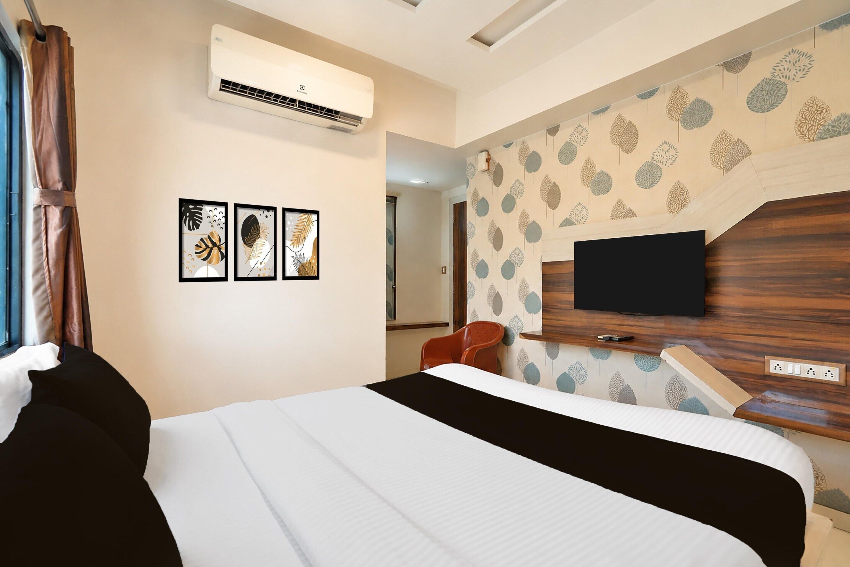 A hotel room with a bed, an air conditioner, a TV, and a chair.