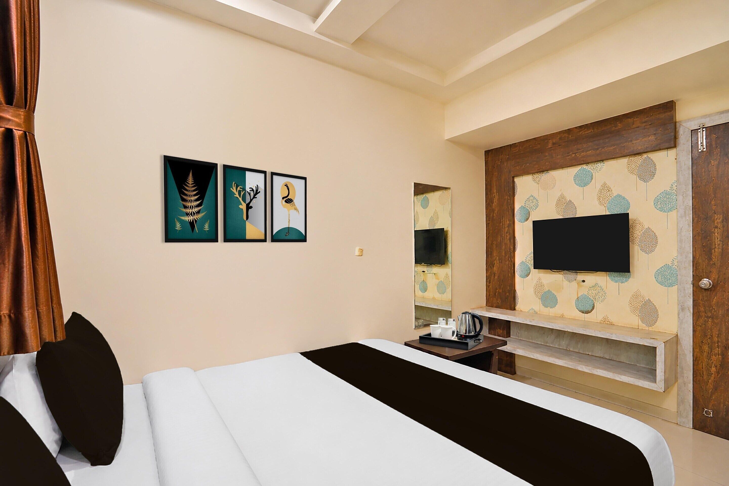Une chambre d’hôtel avec un lit, des œuvres d’art accrochées au mur, un téléviseur fixé sur un panneau en bois et une petite table avec un plateau.
