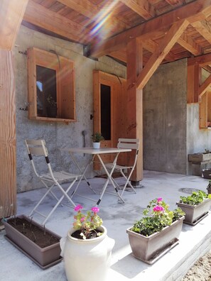 Un área de estar al aire libre techada con vigas de madera, una mesa, sillas y plantas en macetas.