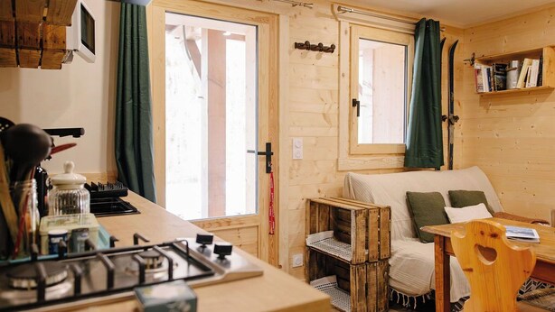 Interior acolhedor de uma cabana, com decoração em madeira, uma kitchenette, um sofá e uma mesa de jantar.