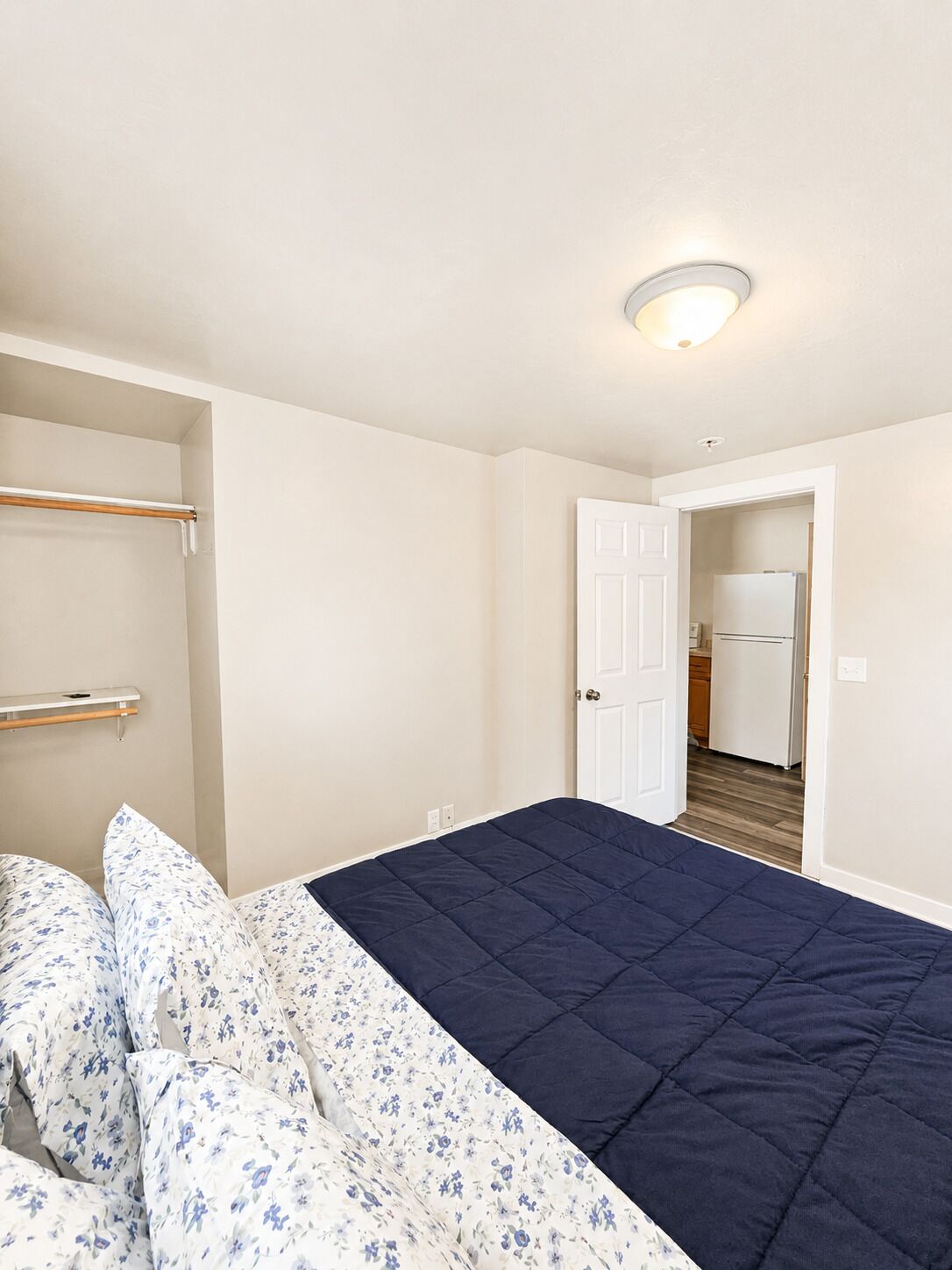 A bedroom with a bed, a wardrobe, and a door leading to a kitchen.