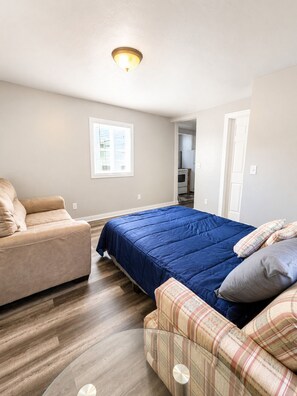 Ein Schlafzimmer mit einem Bett, zwei Sofas, einem Fenster und einer durchgehenden Tür erkennbaren Küche.