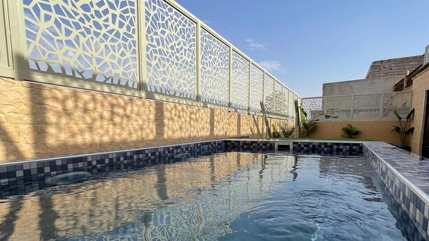 Une piscine dont le fond est recouvert de carreaux disposés selon un motif géométrique, entourée d’un mur orné d’un décor en treillis.