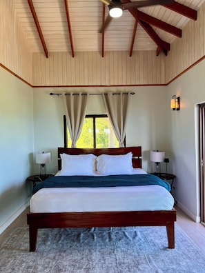 A bedroom with a wooden bed, two bedside tables with lamps, a window with curtains, and a ceiling fan.
