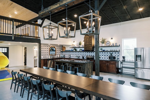 A spacious kitchen with a central island, a dining area with multiple chairs, and a high ceiling with exposed beams.