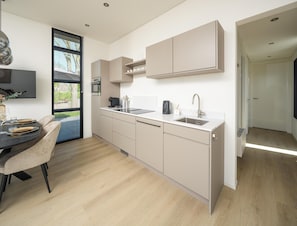 A modern kitchen with a dining area, featuring a built-in oven, a sink, and a dining table with chairs. - Detached 2-guest Home Near Beach (Workum)