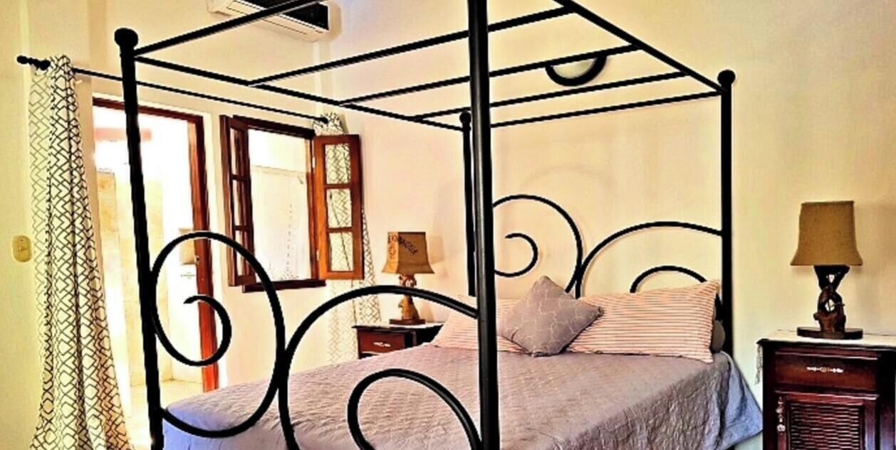 Ein Bett mit Baldachin, ein Nachttisch mit Lampe und ein Fenster mit Vorhängen.