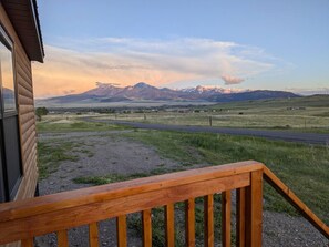 A wooden deck with a view of a road and mountains in the distance. - Mountain Meadow Tiny Cabin (Livingston)