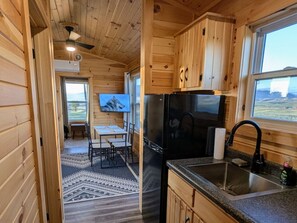 A wooden cabin interior with a kitchen, dining area, and a view of the outdoors. - Mountain Meadow Tiny Cabin (Livingston)