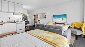 Et moderne hotelværelse med tekøkken, sofa, seng og et maleri af en strand.