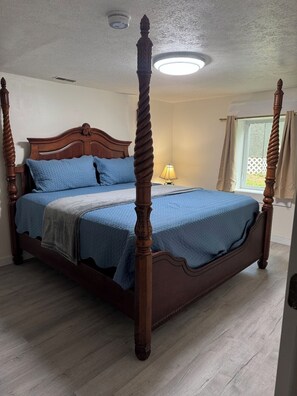 A four-poster bed with a wooden headboard, a bedside lamp, and a window with curtains. - Cozy 1-bedroom basement apt with AC in brilliant Sevierville (Sevierville)