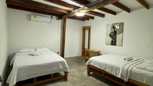 Une chambre avec deux lits simples, un banc en bois, un miroir et un tableau accroché au mur.