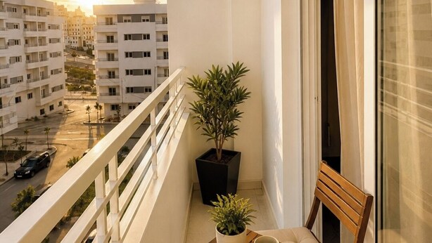 Ein Balkon mit einem Holzstuhl, einem kleinen Tisch, einem Blumentopf und Blick auf Gebäude und eine Straße.