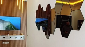 Ein modernes Wohnzimmer mit einem Flachbildfernseher, einer geometrischen Wanddekoration und einem braunen Sofa.