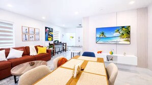 Un soggiorno moderno con zona pranzo, cucina e un grande televisore a parete.