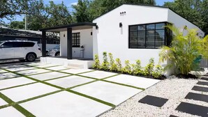 Una casa moderna con un portico coperto, una strada privata e un giardino con piccole piante.