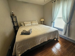 Un lit bien fait, avec une couette blanche, une lampe de chevet et une fenêtre avec des rideaux.