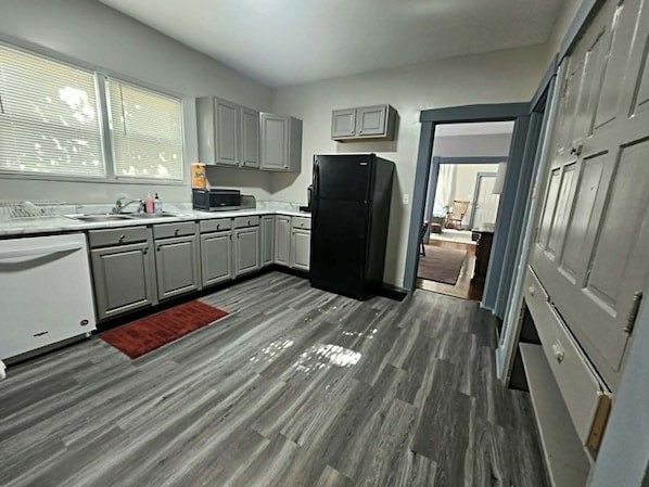 Une cuisine de taille réduite avec des meubles gris, un réfrigérateur noir et un tapis rouge.