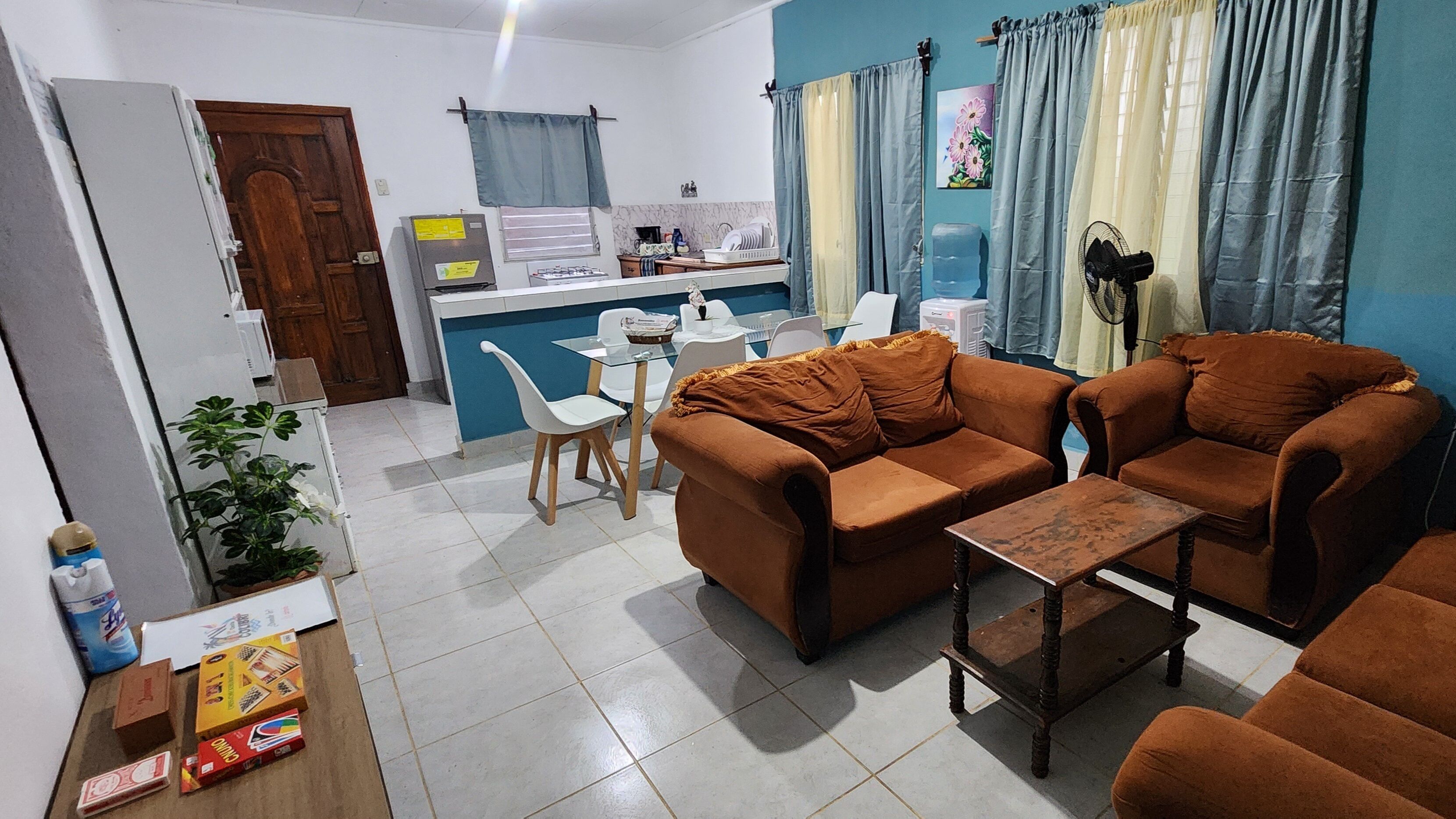 A living room with two brown sofas, a small wooden table, and a white dining table with chairs.