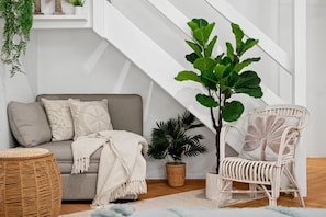 Ein Wohnzimmer mit einer Couch, einem Sessel, einer Pflanze und einer Treppe.