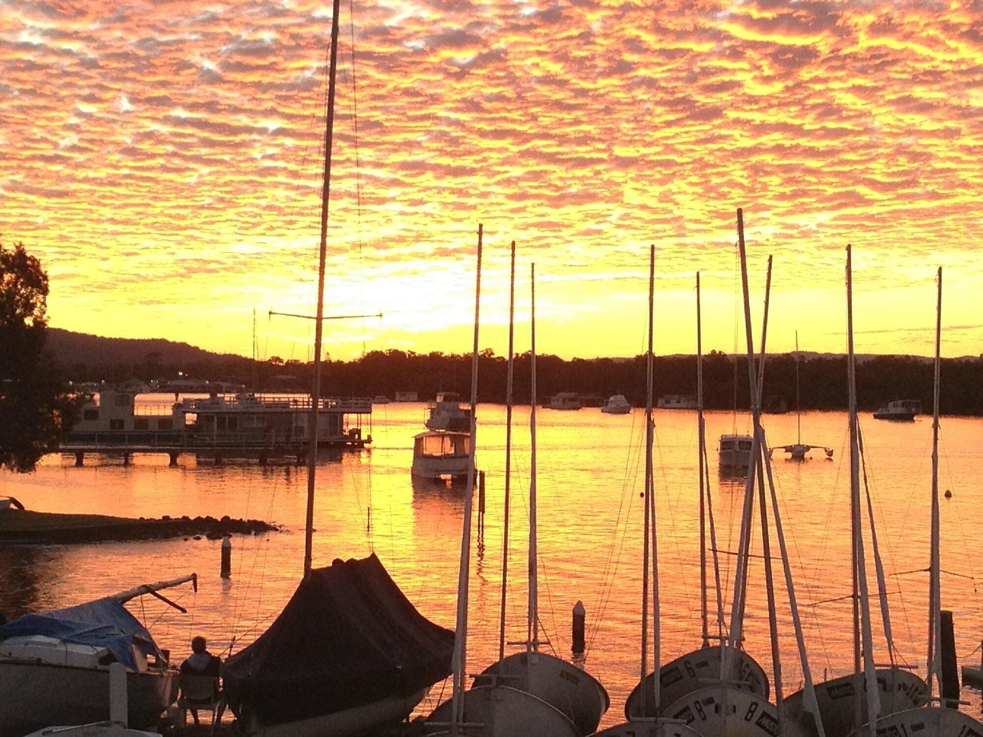 A marina with boats docked, a bridge, and a calm sunset.