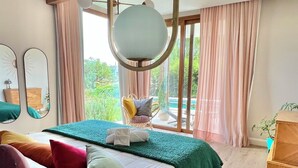 A modern bedroom with a bed, bedside table, and a view of the outdoors.