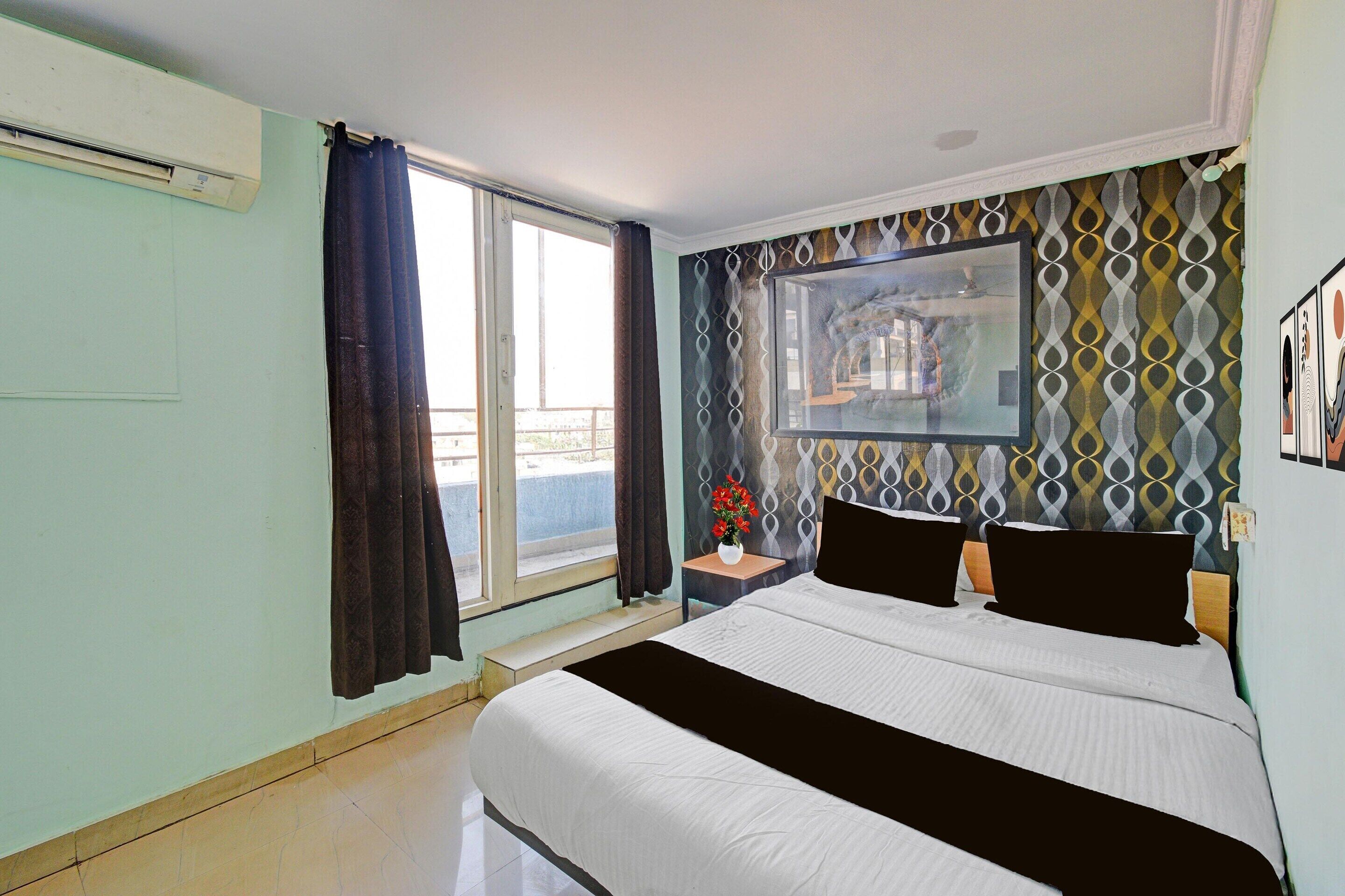 Une chambre à coucher avec un lit, une fenêtre avec des rideaux, un climatiseur fixé au mur et un mur décoré d’un motif.