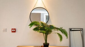 Une table en bois, un pot de fleurs, un miroir rond et un détecteur d’incendie au mur.