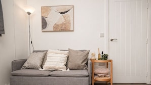 Un salon moderne avec un canapé gris, des coussins à motifs, une lampe sur pied, une petite table d’appoint en bois et une porte.