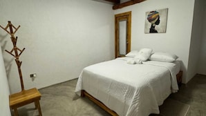 Un dormitori amb un llit, una perxa de fusta, un mirall i un quadre al mur.