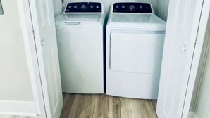 A laundry room with two white washing machines and a dryer, wooden flooring, and white walls.