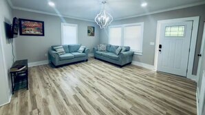 A spacious living room with two sofas, a chandelier, and hardwood flooring.