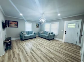 Ein großzügiger Wohnraum mit zwei Sofas, einer Kristallleuchtre und Holzdielen.