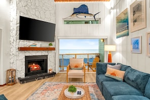 Uma sala de estar com lareira, televisão, vista para o mar, sofá e área de jantar com cadeiras.
