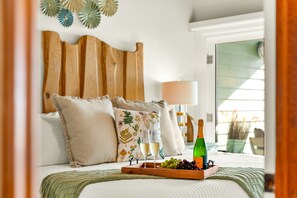 A bedroom with a wooden headboard, a bedside table with a bottle of champagne, glasses, and grapes. - Oceanfront Condo | Rooftop Terrace | Arcades | (Indian Shores)