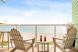 Um alpendre à beira-mar com cadeiras Adirondack, uma mesa com duas garrafas e vista para o oceano.