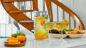 En köksbänk med ett glas apelsinjuice, en tallrik med snacks och ett dekorativt glas.