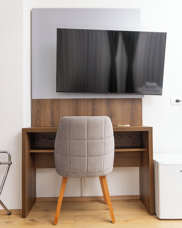 Una habitación moderna con un escritorio de madera, una silla acolchada gris y un televisor de pantalla plana montado en la pared.