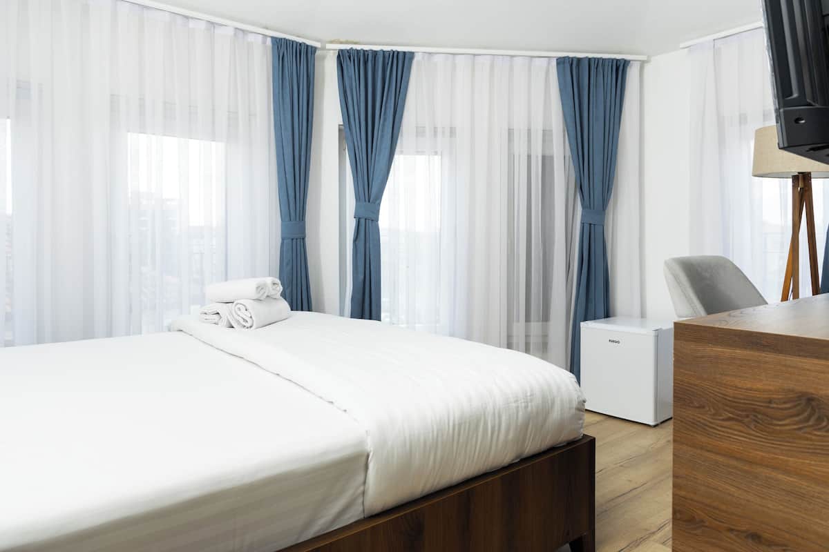 A hotel room with a bed, a desk, a chair, a television, and a small white appliance.