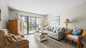 A living room with a sofa, a wicker chair, a cabinet, a coffee table, and a lamp. - Steps to the Sand: Romar Beach 106 (Orange Beach)