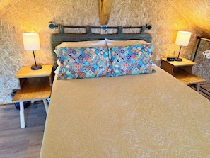 Une pièce chaleureuse avec une tête de lit en bois, un lit agrémenté d’oreillers à motifs, des tables de chevet avec des lampes et un plancher en bois.